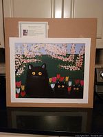 Full view of large unframed fine art print of three black cats by Maud Lewis mounted on cardboard backing, with info card attached.