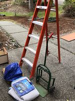 Full view of the orange Louisville 6 ft step ladder, green hand truck, and the collection of tarps, burlap and moving blanket stacked together.