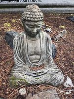 Front view of the concrete Buddha statue seated in meditation on ground covered with mulch and surrounding natural rocks.