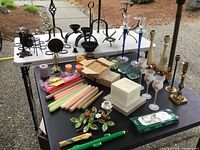 Various candle holders and multiple candle types arranged on tables outside, showing material variety and colors.