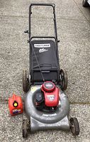 Full view of Craftsman gas lawn mower with grass collection bag and additional red fuel container, showing mower deck, handle, and wheels