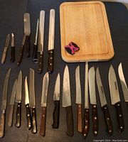 All kitchen knives laid out on a flat surface with the Farberware wooden cutting board and a pink and black handheld sharpener