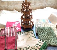 Photo showing the German wood carved nativity tower and the assorted Christmas linens spread around it on a table.