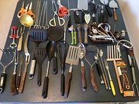 Top view of all kitchen utensils laid out showing variety of tools including knives, spatulas, peelers, corkscrews, and spoons.
