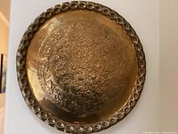 Full front view of circular brass stamped wall art showing intricate floral and leaf patterns with raised border