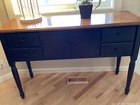 Front view of solid wood buffet showing four drawers, central cabinet, and natural wood top with black base.