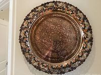 Full view of the large round metal platter mounted on a wall showing overall design and grape motif border.