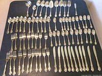 Full view of the flatware set with all pieces arranged on a flat dark surface showing knives, forks, spoons and serving pieces.