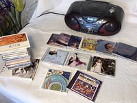 Panasonic CD player with 24 CDs arranged around it, showing variety of album covers and spines, some standing and some laying flat.