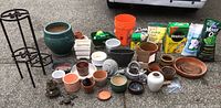 Full lot showing metal 3-tier plant stand, various ceramic planters in multiple sizes and colors, garden figurines, bags of gardening amendments, and small gardening tools and supplies.