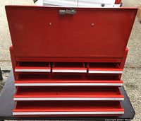 Image showing red metal toolbox with lid open revealing multiple pull-out trays and compartments inside.
