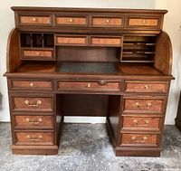 Front view of roll top desk with the top open, showing green marble inlay on desktop and multiple drawers with brass handles.