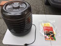 Photo of a black plastic Ronco food dehydrator with stacked trays, a clear round lid, and a power cord on a white table outside.