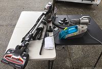 Shark Rocket DuoClean upright vacuum, attachments, Dirt Devil handheld spot cleaner, Euro-Pro handheld vacuum on tables.