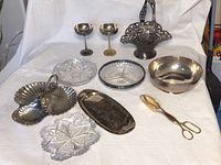 Overall view of lot on white cloth showing sterling bowl at right, cut glass trays at center and plated serving pieces surrounding