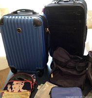 Front view of large blue hard shell suitcase and black hard shell carry-on suitcase with black duffel bag and makeup bags on table
