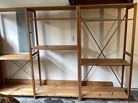 Front view of two wooden shelving units showing three shelves on large unit and two shelves on smaller unit along with metal braces and visible wear.