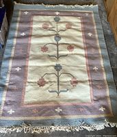 Full view of the rectangular woven area rug showing the central floral pattern and colored border with tassels on one end.