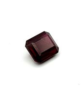 Red ruby gemstone, step cut rectangular shape shown against plain white background at an angle.