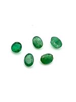 Five small faceted emerald gemstones shown on white background, displaying green color and varying shapes.