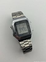 Front view of the Casio digital watch showing time, date, and day with stainless steel linked band.