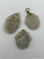 Three Chinese jade pendants shown from top view, two with metal bales, one without. Carved motifs resembling leaves or natural shapes visible.