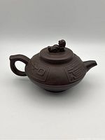 Front and side view of the Chinese Yixing purple clay teapot showing the sculpted figure on the lid and embossed Chinese characters on the body.