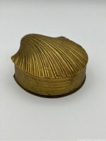 Brass clamshell trinket box closed showing textured shell lid and round body.
