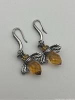 Front view of the pair of bee-shaped dangle earrings with orange crystal body and silver wings and hooks on white background.