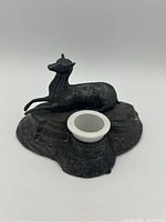 Angled view of the metal inkwell with deer figure and porcelain insert showing overall form and details.