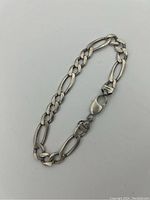 Full view of the sterling silver Figaro chain bracelet with visible large flat and round links laid out flat.