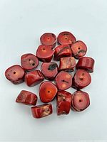 Close-up photograph showing large red coral beads with natural shapes, holes drilled for stringing, and color variations.