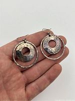 Earrings held in hand showing front design with circular hammered discs inside wire hoops