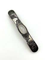 Front view showing bar-shaped sterling silver hair clip with engraved floral patterns and an oval moonstone cabochon in the center.