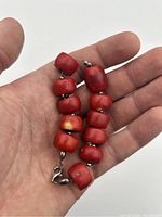 Bracelet held in hand showing details of red coral beads and clasp.