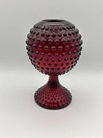Front angled view of a red hobnail glass mug or vase showing spherical body and flared hobnail footed base.