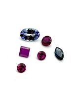 Top-down close-up photo showing two blue sapphires and four rubies arranged on a white surface, highlighting their colors and cuts.