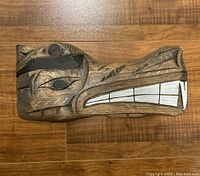 Front and side view of the carved wooden piece featuring painted teeth, eye, and facial patterns.