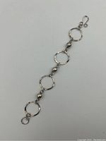 Full view of the sterling silver bracelet laid flat showing four large textured oval rings alternating with small round silver beads and the hook clasp on a plain white background.