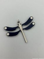 Front view of the dragonfly pendant showing blue enamel wings with white circular accents and polished silver body.