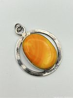 Front view of a circular sterling silver pendant with a bright orange oval stone centered inside it. Loop bail is attached for hanging. Pendant ring is plain with slight surface texture.
