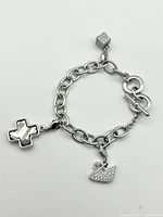 Full view of silver-tone charm bracelet with three charms and toggle clasp on white background.