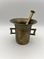 Photo showing the mortar with pestle resting inside and visible wide flared rim and rectangular handles.