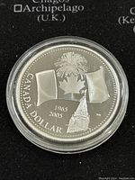 Reverse side of coin showing commemorative design with maple leaf, flags, years 1965 and 2005, and building