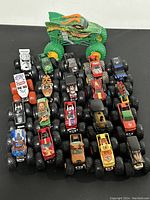 Overview of 21 die cast monster trucks arranged in rows, showing variety of designs and the prominent green dragon truck at the back.