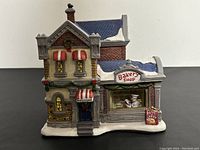 Front view of porcelain Christmas village bakery shop with snow on roof and holiday decorations.