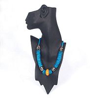 Full view of the necklace on a black bust showing turquoise-colored disc beads, black and white patterned dyed bone beads, and a central amber bead.