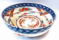 Angled side view of the antique Asian hand painted porcelain bowl showing blue lattice rim and colorful floral motifs inside bowl.