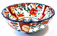 Angled front view showing scalloped rim, detailed floral and geometric hand painted design with vivid reds, oranges, blues and greens on porcelain bowl.