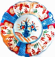 Top view showing the colorful hand-painted floral design on the scalloped edge plate, highlighting red, blue and orange colors with central blue vase and flower motif.